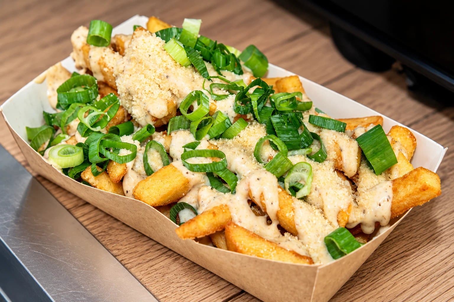 Bakje friet met een romige saus, geraspte kaas en verse lente-ui