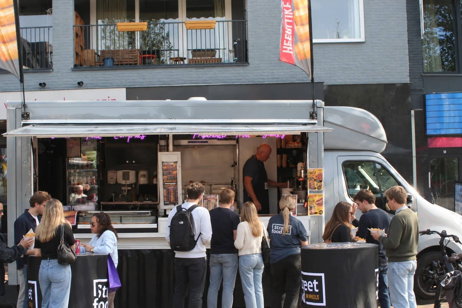 De foodtruck van Street food on Wheels op de markt, met het luik open, roze neonletters en een rij klanten voor de toonbank