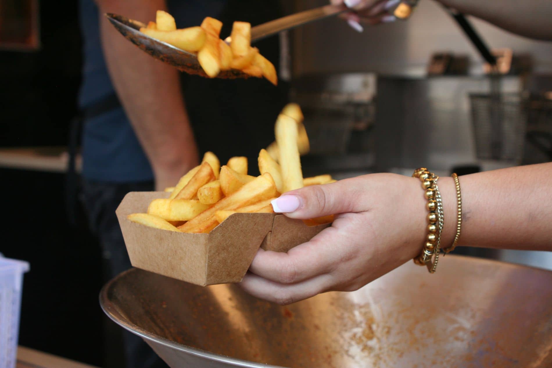 Friet wordt met de schep in een kartonnen bakje gedaan