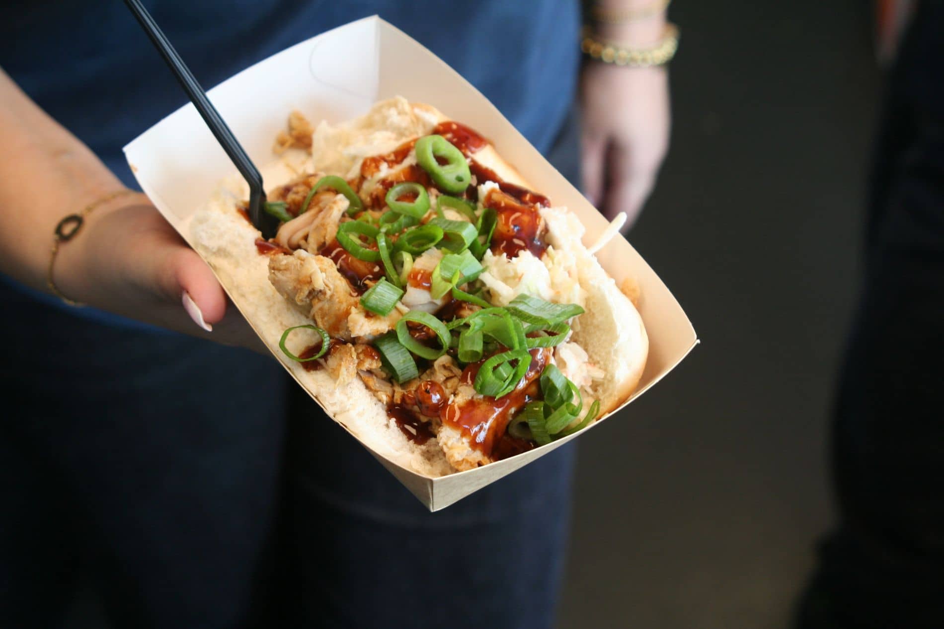 Een broodje pulled chicken met lente-ui en barbecuesaus, vastgehouden in een bakje