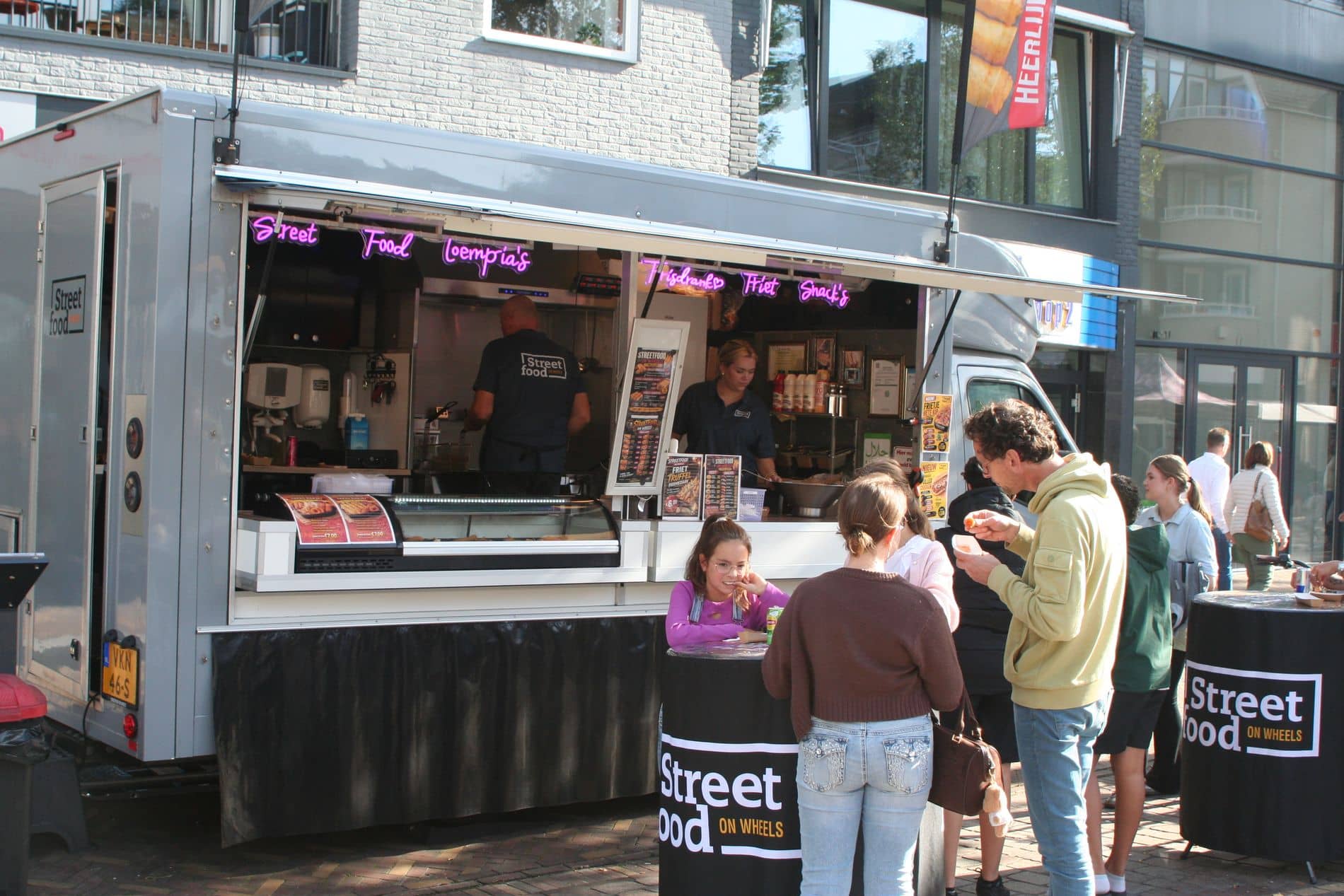 Klanten bij de toonbank van de foodtruck, met kinderen en een statafel