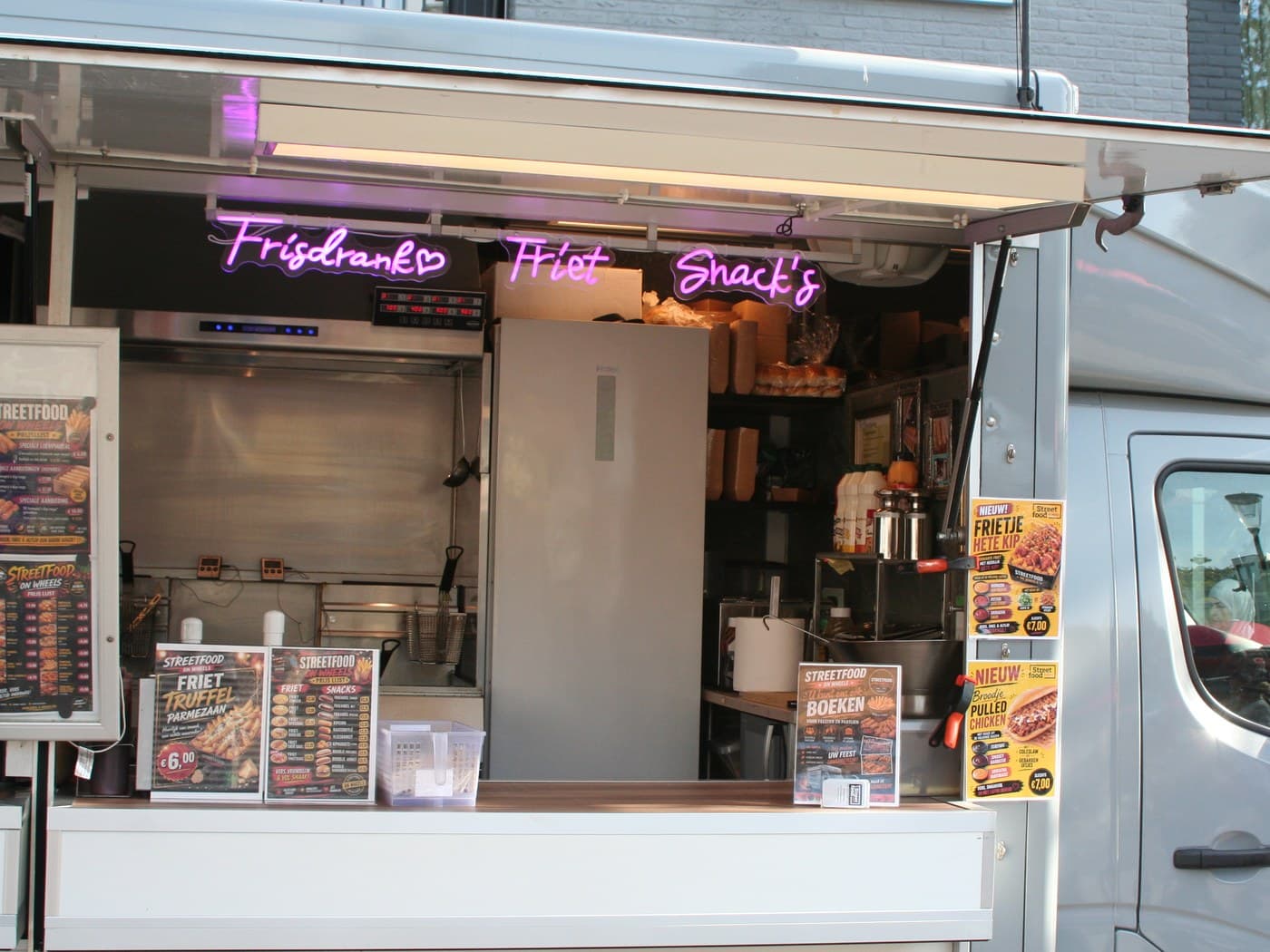 De open foodtruck met de roze neonletters Frisdranks, Friet en Snack's en de prijsborden op de toonbank
