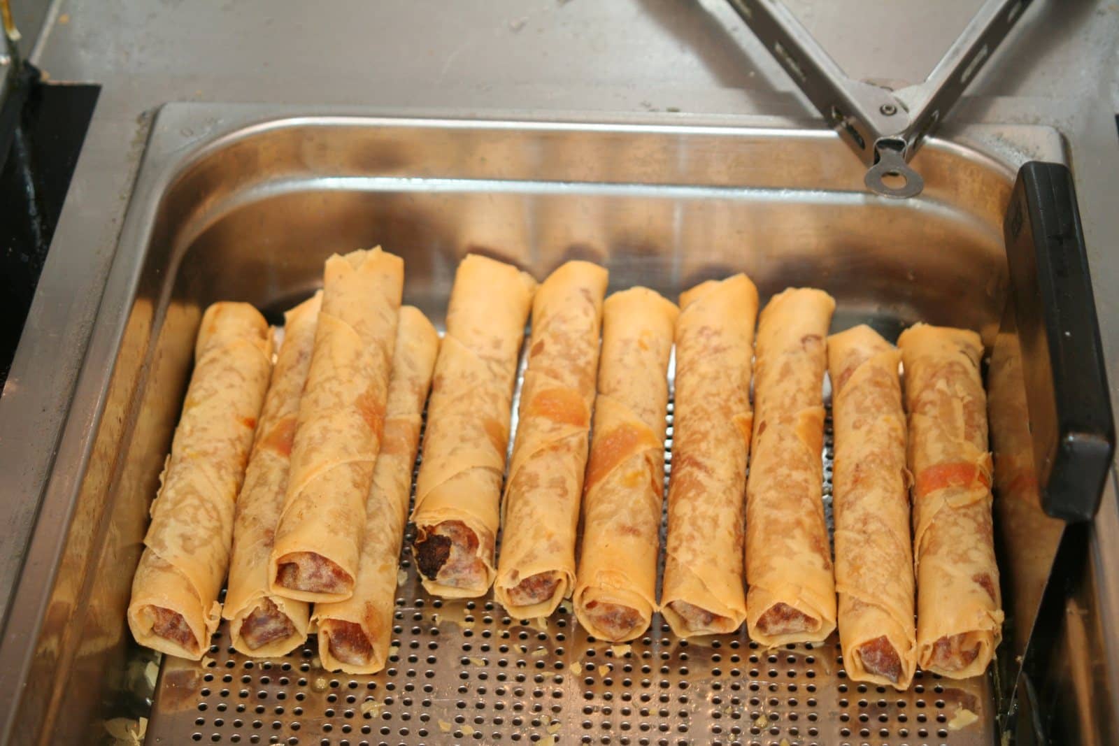 Een rij gebakken loempia's, goudbruin en knapperig, in de bakbak