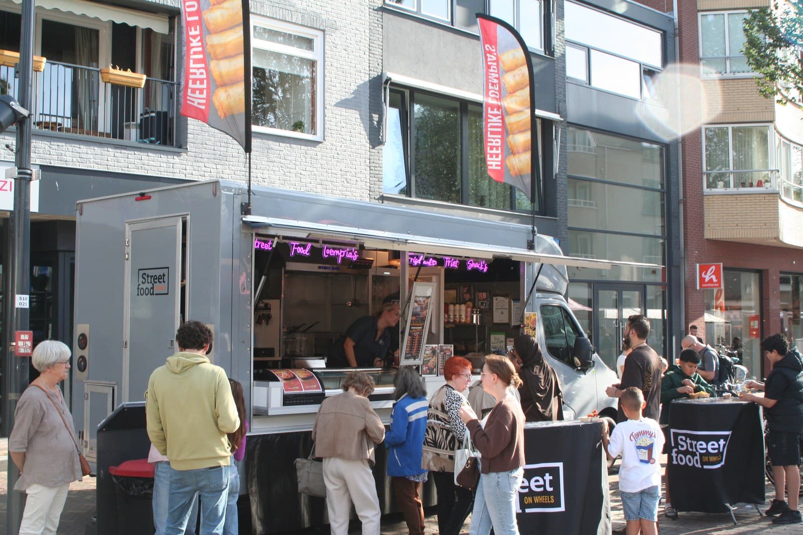 De hele foodtruck op de markt, met klanten aan de toonbank en vlaggen langs de gevels